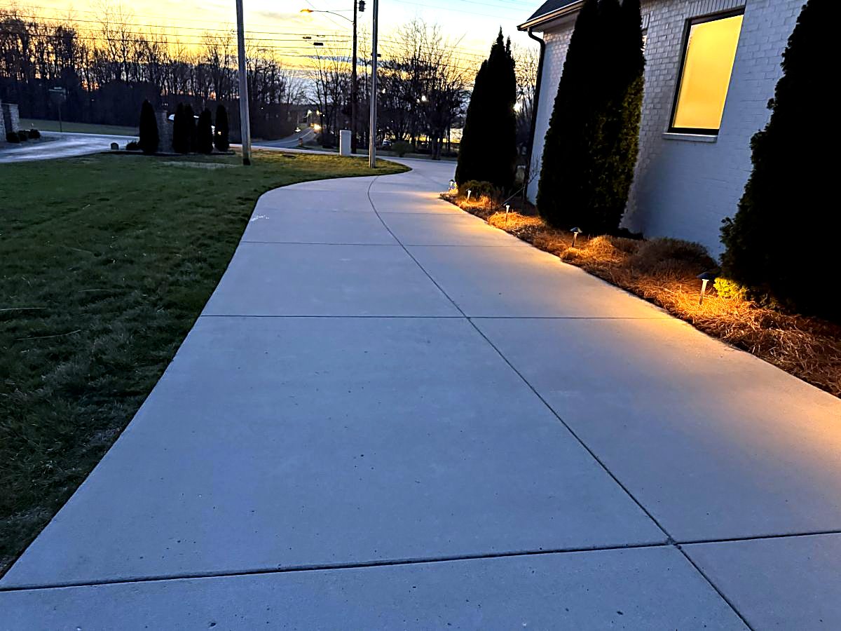 Clean concrete walkway along a white brick house at dusk